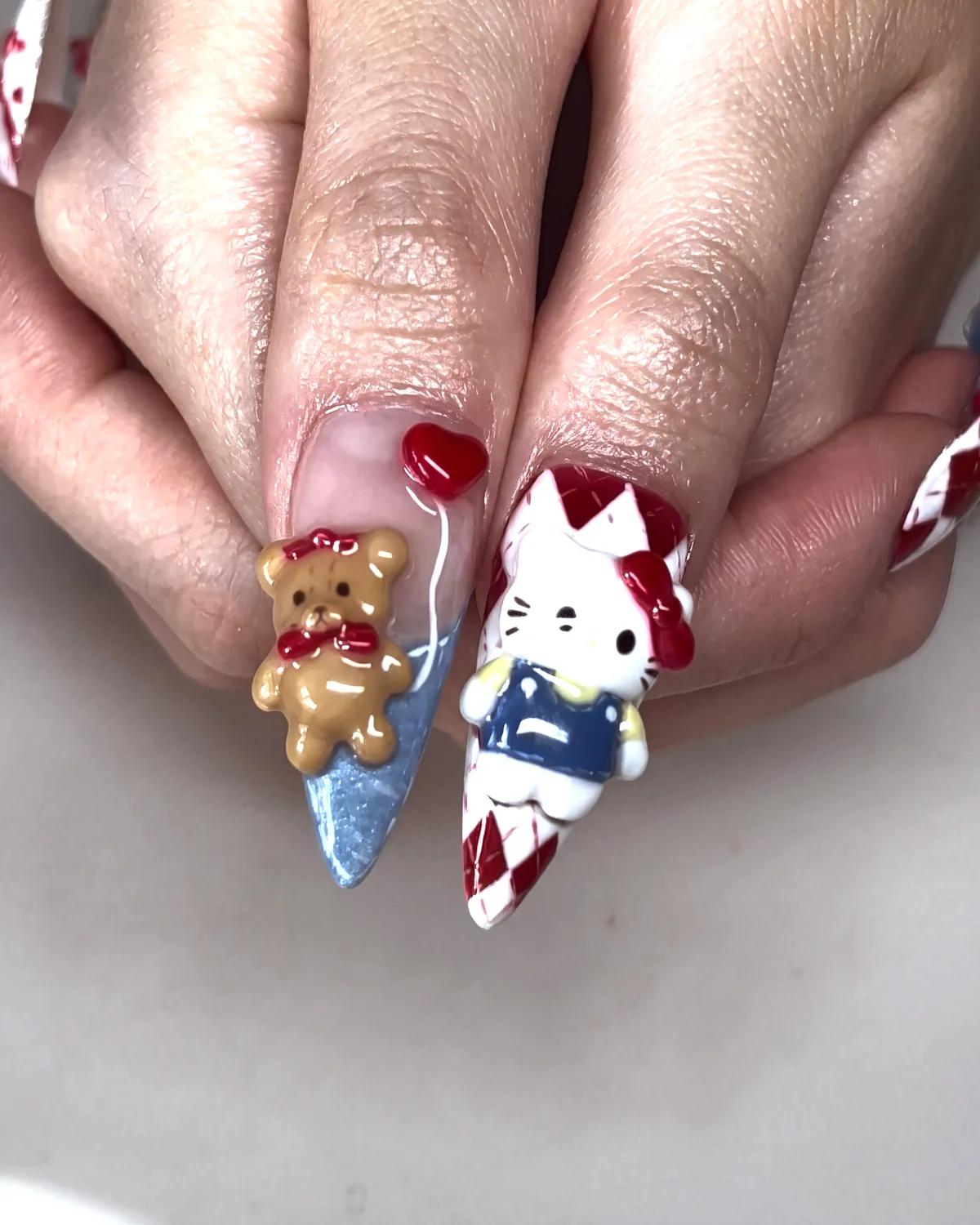 Hello Kitty in blue overalls and a tan bear sculpted on XL stiletto nails, one argyle, one blue cat-eye